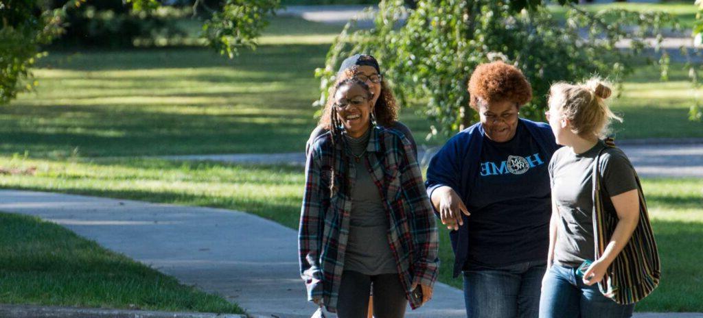 Four women walking together on campus laughingh and smilinng.